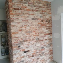 Usługi Remontowo-Budowlane Jarosław Drozd - Ściana wyłożona dekoracyjną cegłą w odcieniach czerwieni i bieli, widoczne niedokończone prace wykończeniowe przy podłodze i ścianie obok.