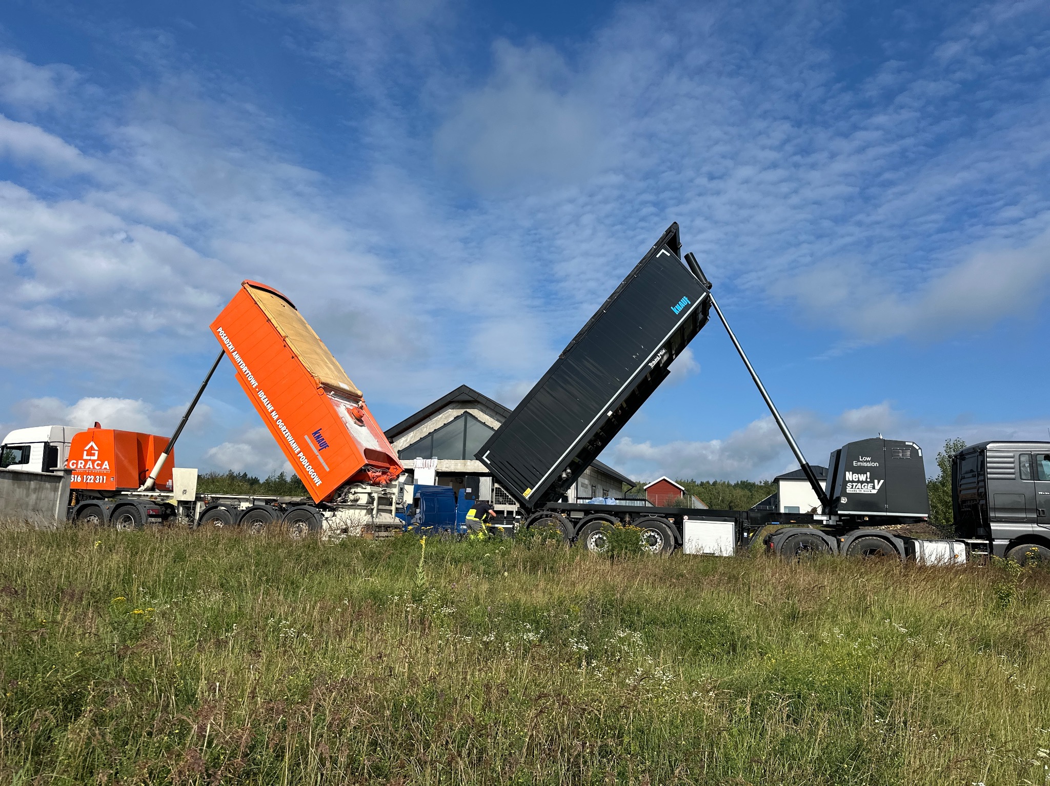 Dwa zestawy do wylewek anhydrytowych Knauf na tle budowy domu jednorodzinnego, jeden pomarańczowy, drugi czarny, w trawie, pod błękitnym niebem.