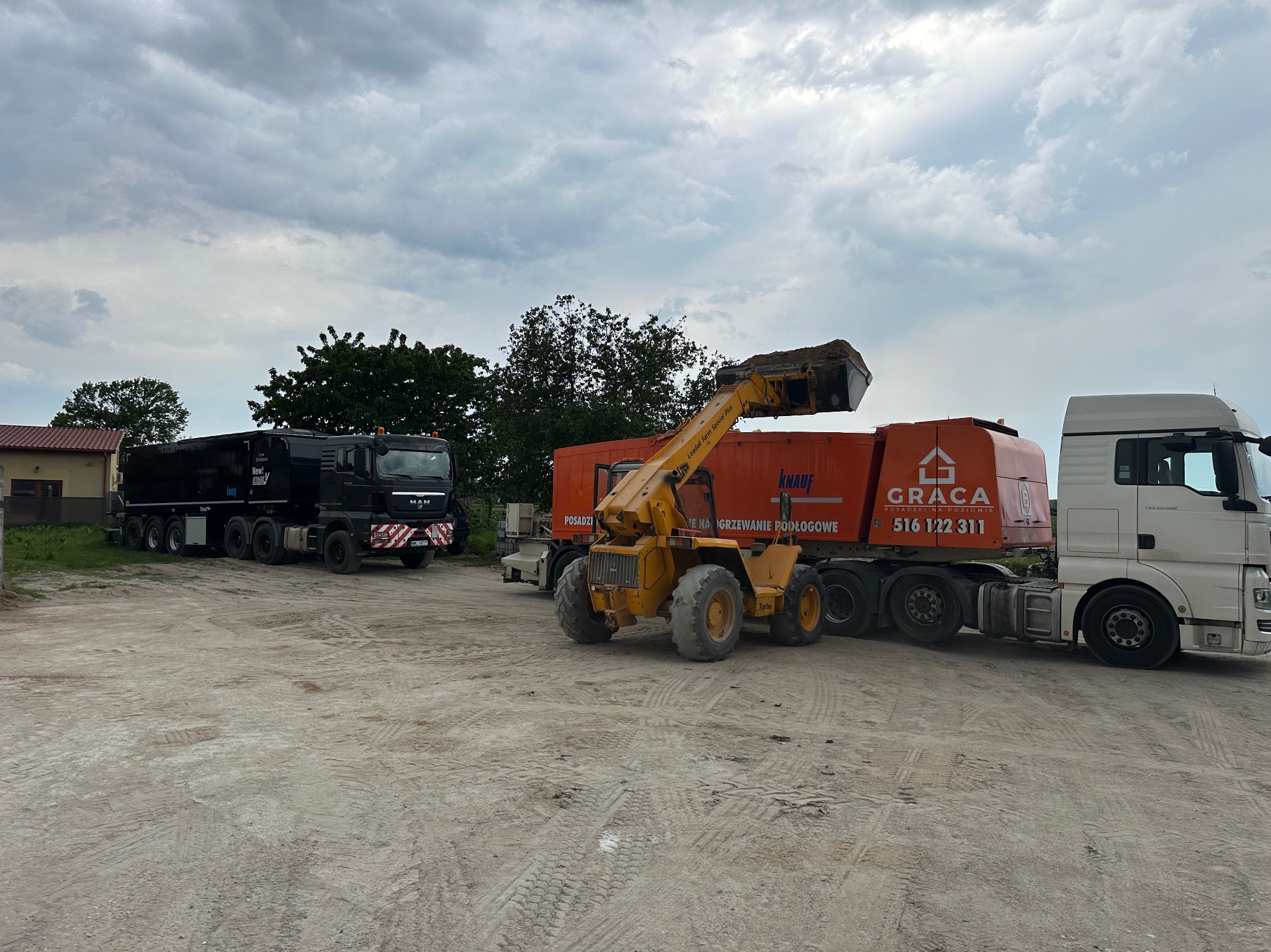 Ciężarówka i ładowarka teleskopowa Knauf na placu budowy. Sprzęt do wylewek, widoczne oznaczenia 'Posadzki na poziomie' i 'Ogrzewanie podłogowe'.