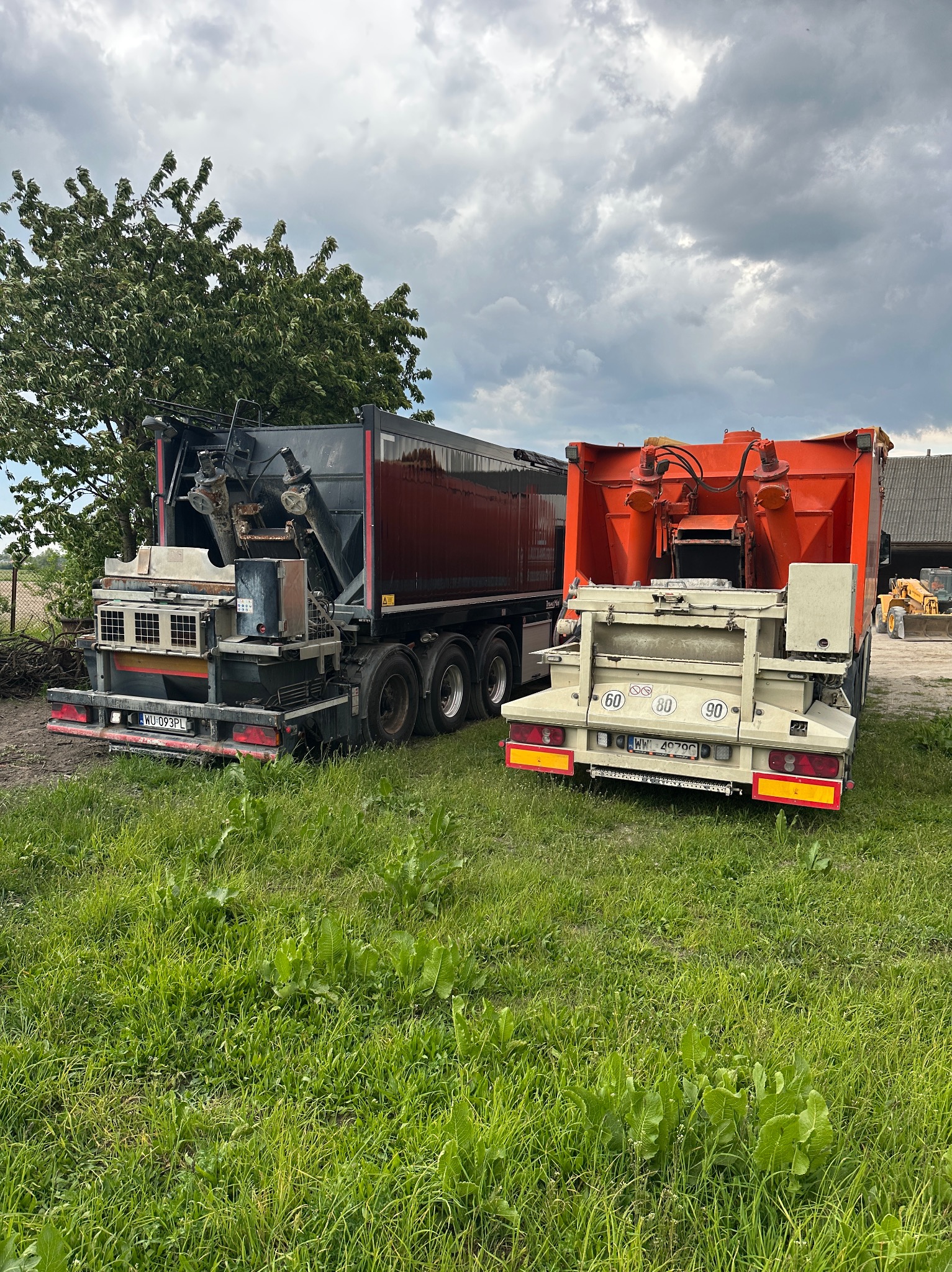 Dwa specjalistyczne pojazdy do wylewek na trawiastym terenie, z widocznymi elementami mieszającymi i pompującymi, pod pochmurnym niebem.