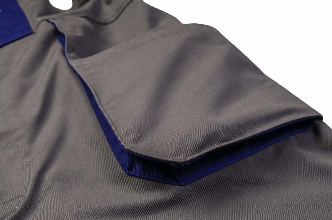Szczegół kieszeni na szarej odzieży roboczej z granatowym wykończeniem, widoczny fragment kołnierza.