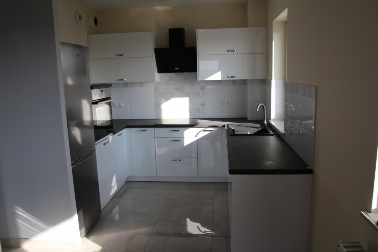 Nowoczesna biała kuchnia z czarnym blatem i płytkami w geometryczne wzory, oświetlona naturalnym światłem z okna.