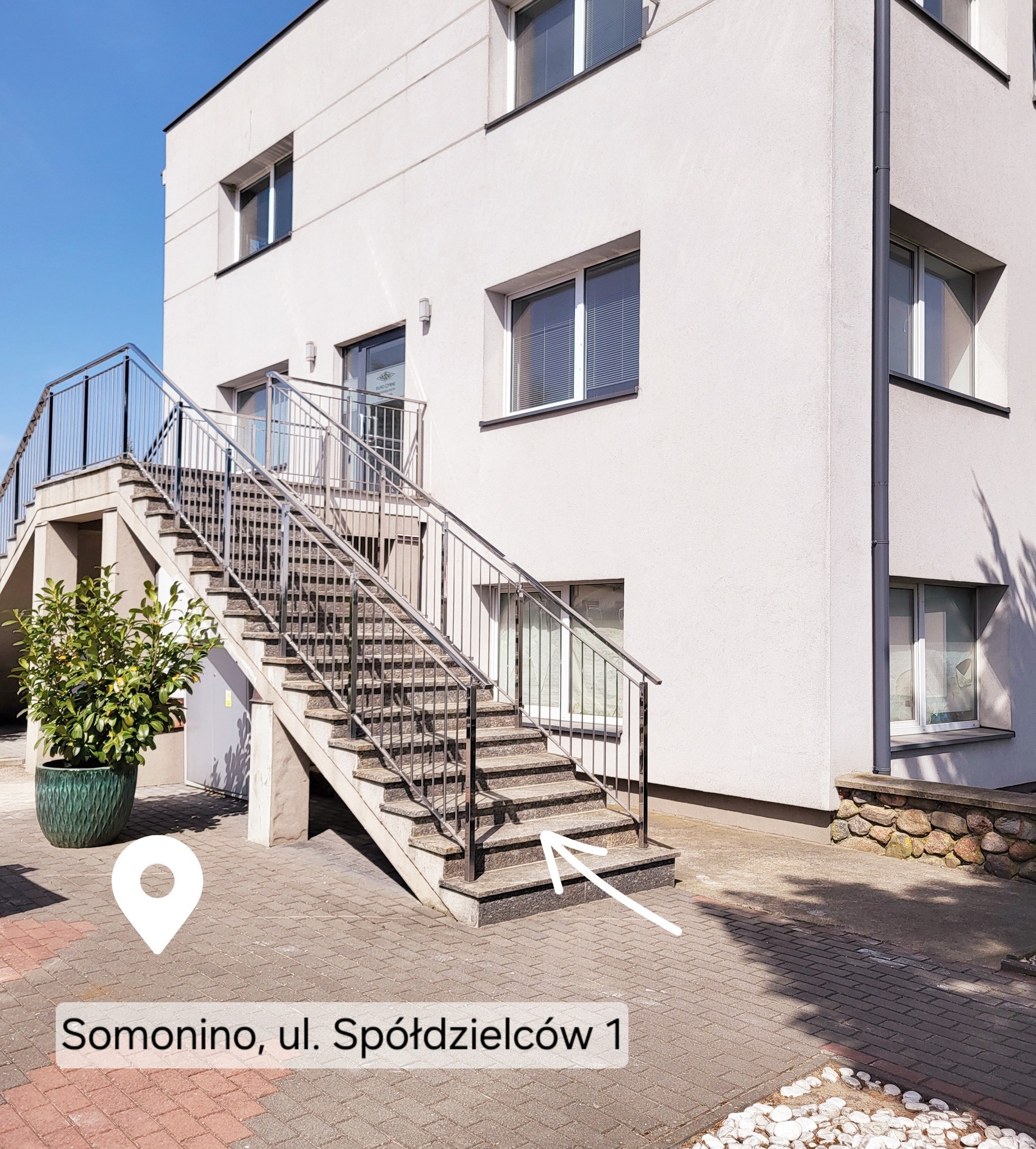 Biały budynek biurowy z metalowymi schodami i zielenią, adres Somonino, ul. Spółdzielców 1, sugerujący siedzibę firmy.