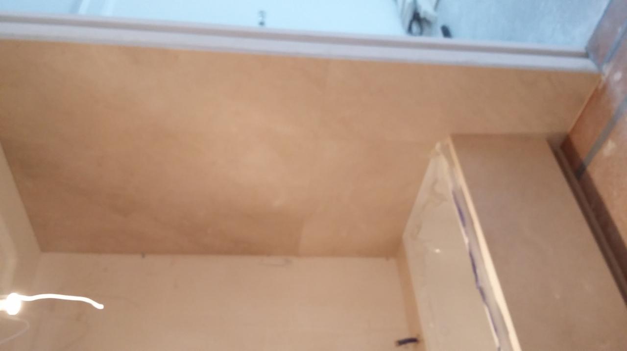 Beżowy blat w łazience, zamontowany pod oknem, widoczne niedoskonałości w wykończeniu ściany.