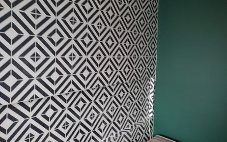 Ściana wyłożona czarno-białymi płytkami o geometrycznym wzorze, sąsiadująca z gładką, zieloną ścianą w Lublinie. Widoczny fragment poduszki w dolnym rogu.