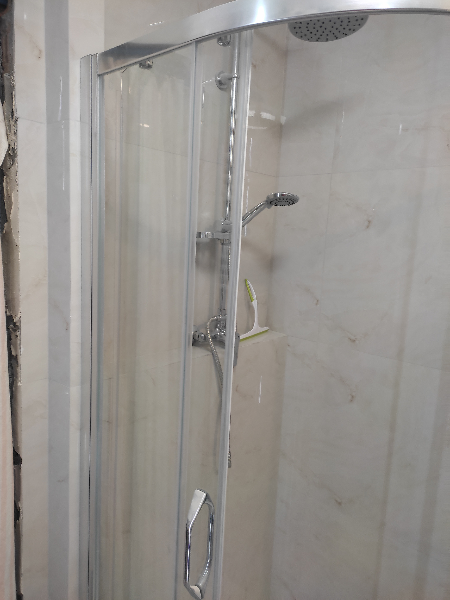 Kabina prysznicowa z chromowanymi detalami i marmurowymi płytkami w tle. Widoczny fragment ściany w trakcie wykończenia.