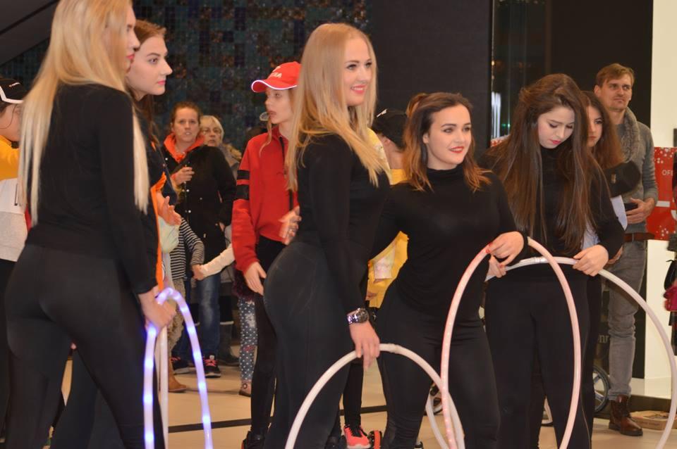 Grupa młodych kobiet w czarnych strojach trzymających świecące hula-hoop, przygotowujących się do występu na tle publiczności.