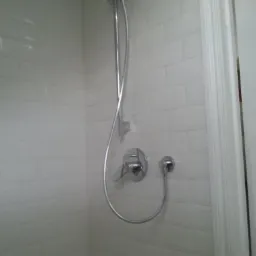 Biała łazienka z chromowaną baterią prysznicową i białymi, prostokątnymi płytkami na ścianach.