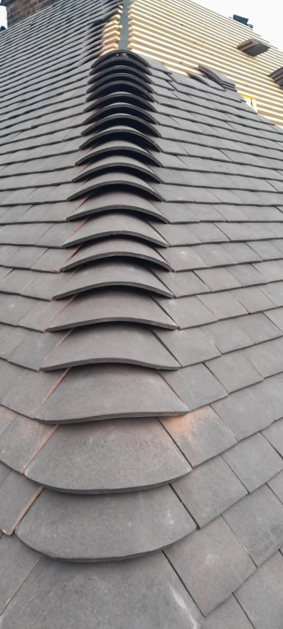 Ułożone dachówki ceramiczne w odcieniach szarości, z widoczną strukturą i charakterystycznym wzorem łuski. Częściowo widoczne drewniane elementy konstrukcji dachu.