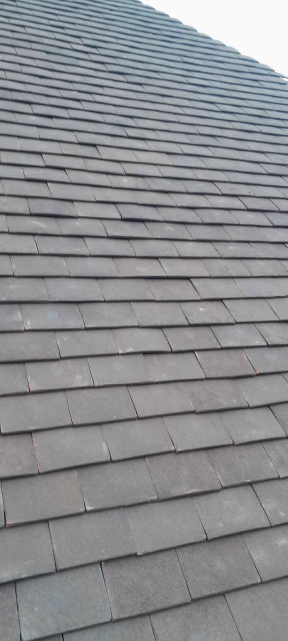 Szczegółowe ujęcie szarej, ułożonej dachówki na skośnym dachu, z widoczną fakturą materiału i regularnym wzorem pokrycia.