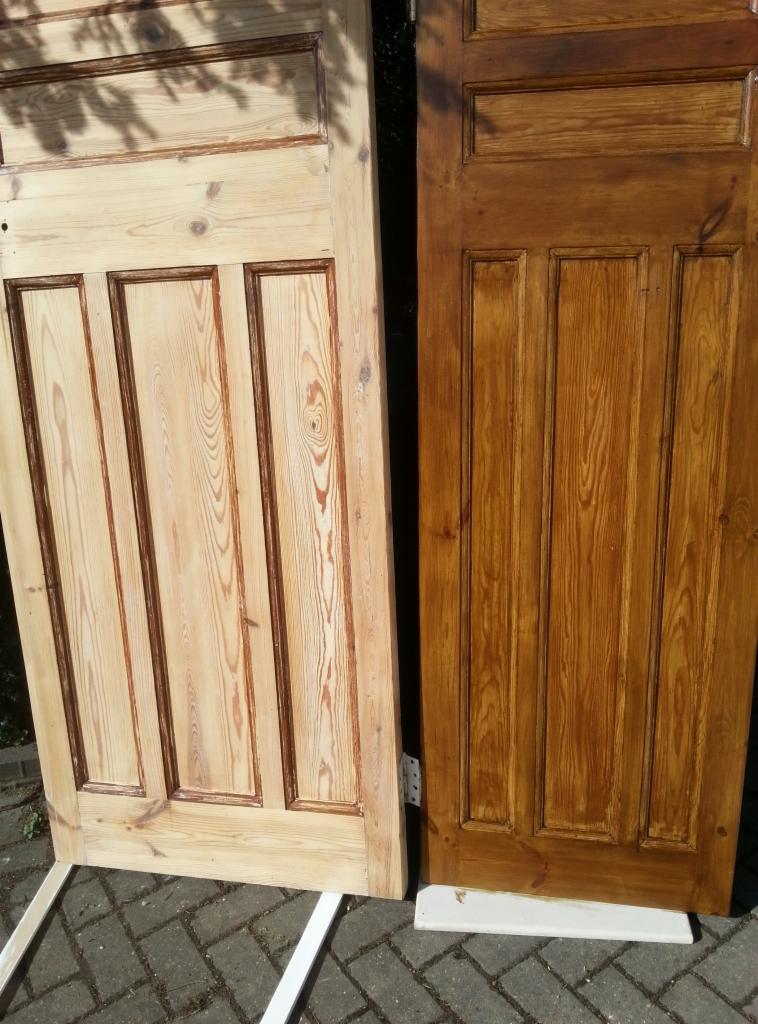 Dwie drewniane drzwi panelowe: jedna surowa, jasna, druga bejcowana na ciepły brąz, o widocznej strukturze drewna, oparte o siebie na zewnątrz, na kostce brukowej.