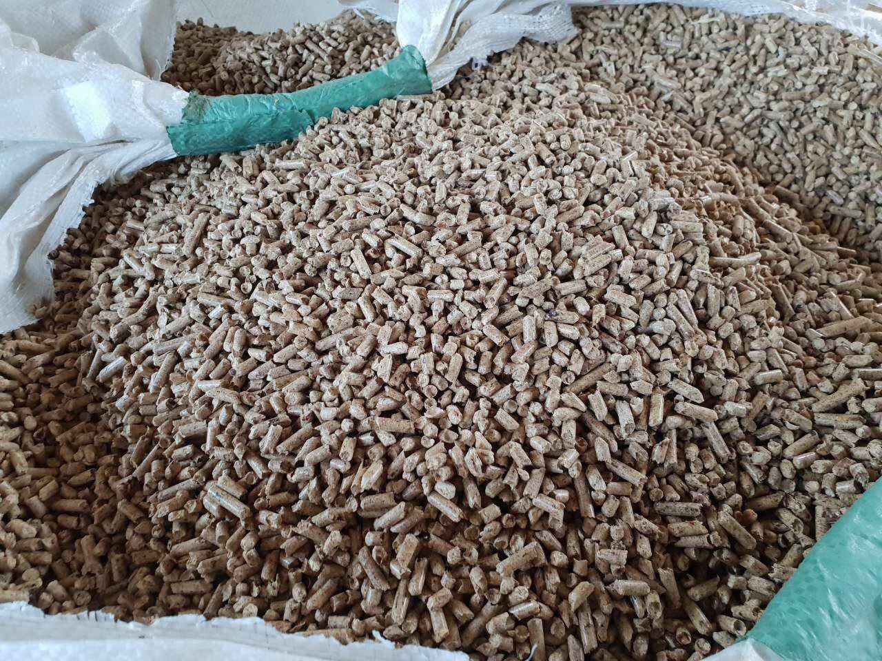 Worek wypełniony jasnobrązowym granulatem opałowym, widoczne fragmenty worka z zielonymi elementami. Granulat o cylindrycznym kształcie.