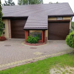 Dwustanowiskowy garaż z brązowymi, zwiniętymi roletami zewnętrznymi, brązowym dachem z dachówki i kostką brukową na podjeździe.