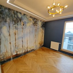 Mochocki Piotr - Pokój po remoncie: parkiet w jodełkę, ściana z motywem leśnym, nowoczesna lampa, listwy LED pod sufitem, okno z widokiem na miasto. Nowoczesne wykończenie.