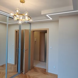 Mochocki Piotr - Nowoczesne wnętrze z parkietem w jodełkę, przesuwną szafą z lustrem i designerską lampą sufitową. Oświetlenie LED podkreśla geometrię sufitu.
