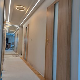 Mochocki Piotr - Korytarz po remoncie z drewnianymi drzwiami z przeszkleniami i oświetleniem LED na suficie. Podłoga zabezpieczona folią malarską.