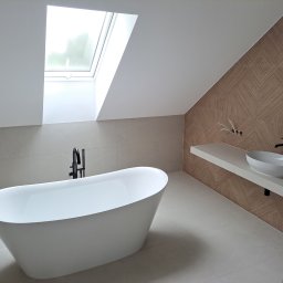 Mochocki Piotr - Nowoczesna łazienka na poddaszu z wolnostojącą wanną, umywalką na blacie i oknem dachowym. Beżowe płytki i geometryczny wzór na ścianie dodają elegancji.