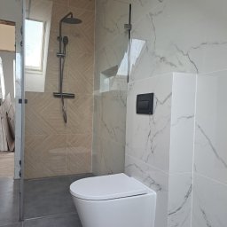 Mochocki Piotr - Nowoczesna łazienka z kabiną prysznicową typu walk-in, wiszącą toaletą i marmurowymi płytkami. Uwagę zwraca okno dachowe nad prysznicem.