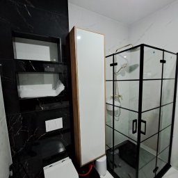 Mochocki Piotr - Nowoczesna łazienka z czarnymi marmurowymi płytkami, kabiną prysznicową z czarnymi ramami i wiszącą szafką. Uwagę przykuwa kontrast bieli i czerni.