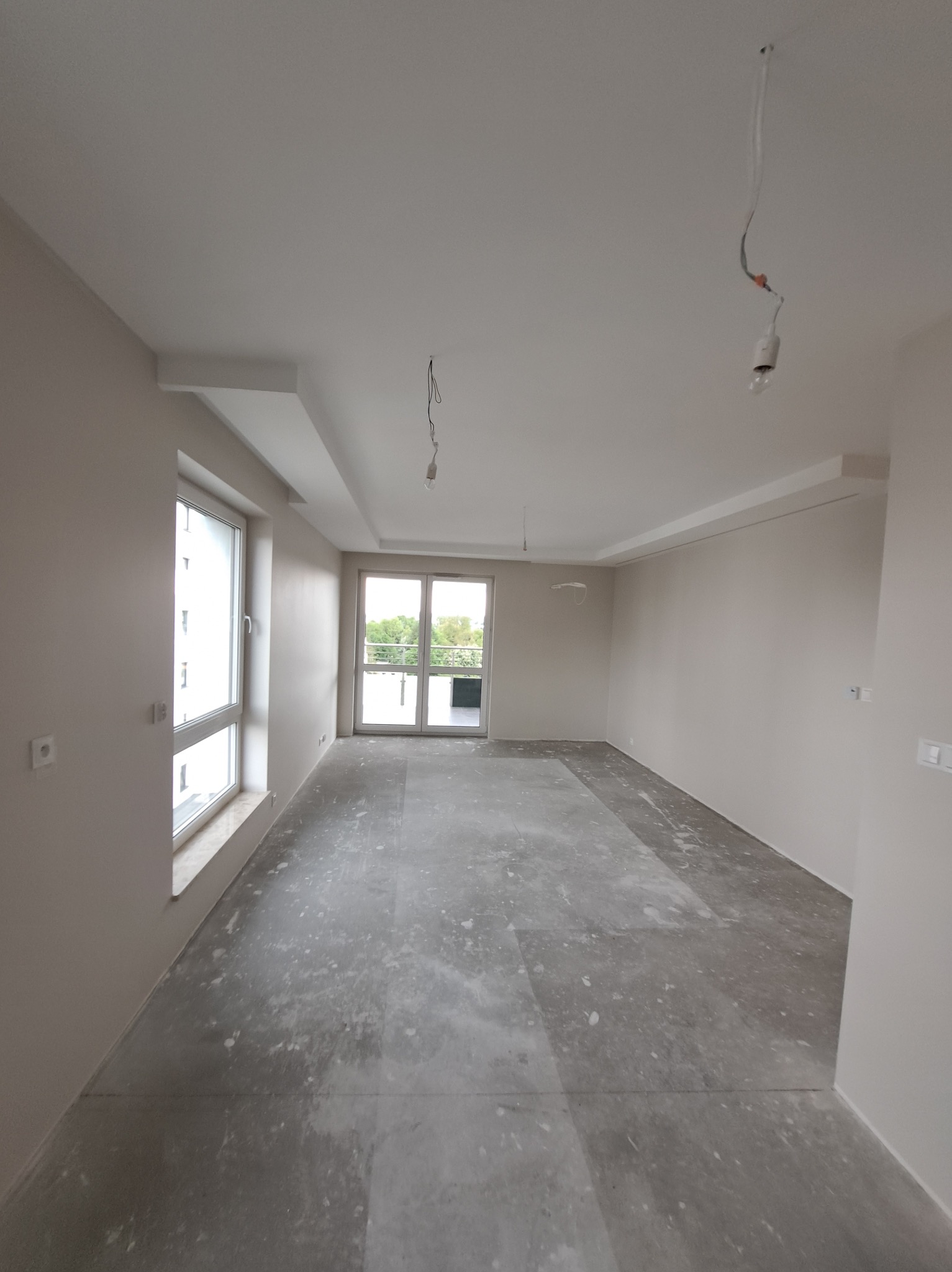 Wnętrze pokoju po szpachlowaniu ścian i sufitu, przygotowane do dalszych prac wykończeniowych. Widoczne okno i drzwi balkonowe.