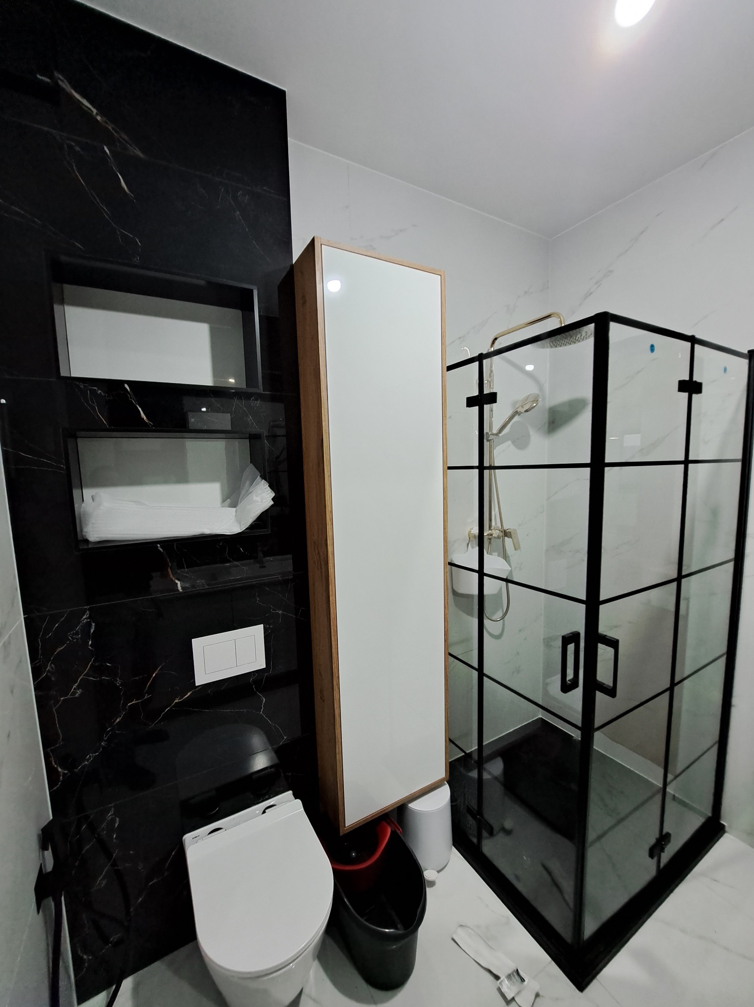 Nowoczesna łazienka z czarnymi marmurowymi płytkami, kabiną prysznicową z czarnymi ramami i wiszącą szafką. Uwagę przykuwa kontrast bieli i czerni.
