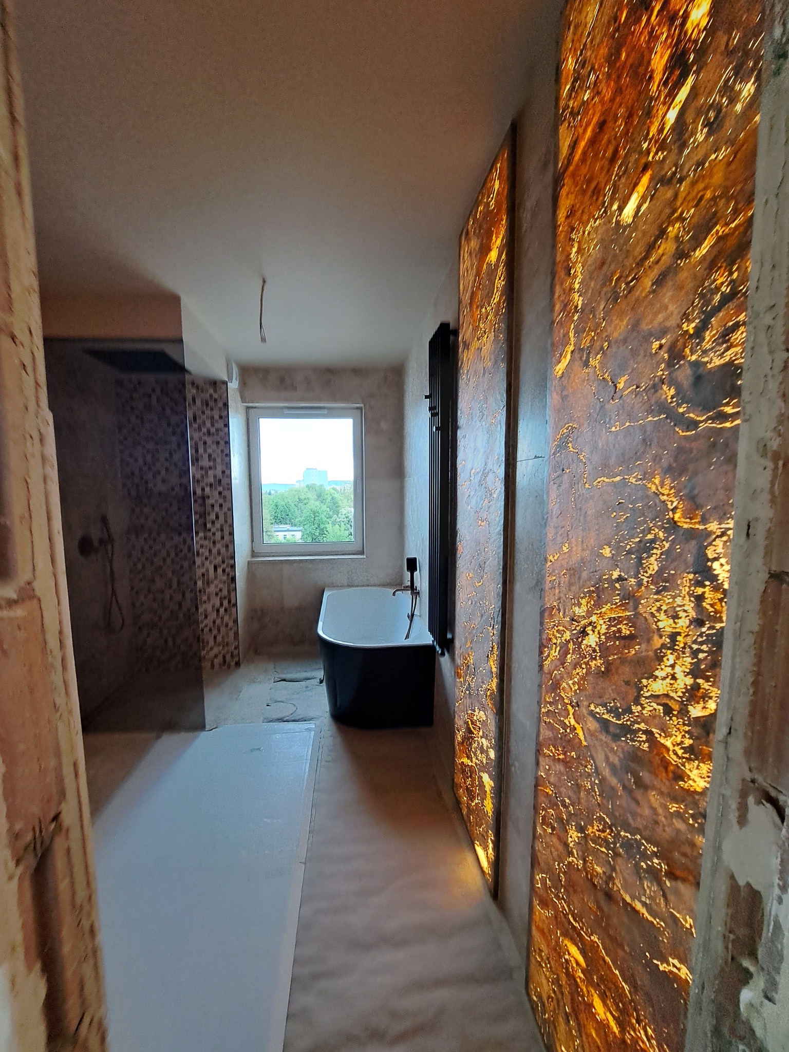 Łazienka w trakcie remontu: czarna wanna, mozaika pod prysznicem i podświetlane panele dekoracyjne z efektem onyksu na ścianie. Widoczne surowe ściany i podłoga.