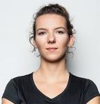 Portret kobiety z włosami upiętymi do tyłu, ubrana w czarną koszulkę, na jasnym, neutralnym tle.