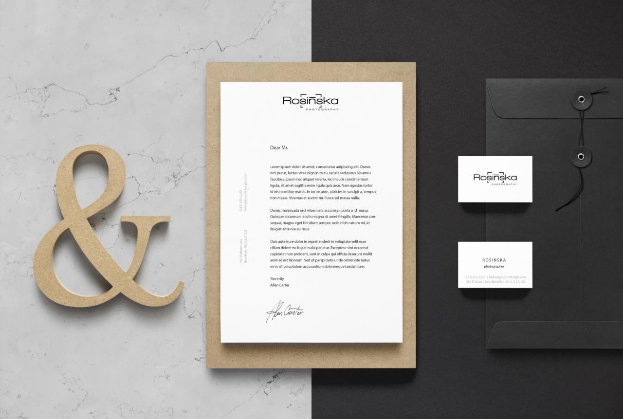 Identyfikacja wizualna fotografa: list firmowy, wizytówka i koperta na ciemnym tle, uzupełnione drewnianym znakiem '&' na marmurowej powierzchni.