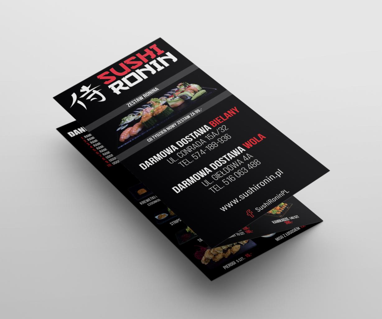 Czarna ulotka reklamowa Sushi Ronin z zestawami sushi, adresami dostawy w Bielanach i Woli oraz danymi kontaktowymi, leżąca na jasnym tle pod kątem.