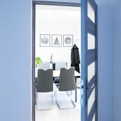 Otwarty widok na salę konferencyjną z geometrycznymi obrazami na ścianie, widoczny przez uchylone drzwi w kolorze ciemnego drewna z przeszkleniami.