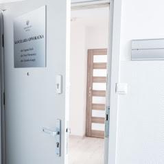 Tabliczka informacyjna na drzwiach wejściowych do kancelarii z napisem 'Kancelaria Opolska', widoczny fragment wnętrza z drzwiami i elementami wyposażenia.