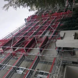 Budynek w trakcie remontu z rusztowaniami, bluszcz oplatający ściany, widok z dołu na elewację.