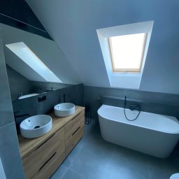 USŁUGI BUDOWLANE GRZEGORZ DZIERGAS - Nowoczesna łazienka na poddaszu z dwoma umywalkami nablatowymi na drewnianej szafce, wolnostojącą wanną i oknem dachowym.