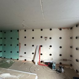 USŁUGI BUDOWLANE GRZEGORZ DZIERGAS - Montaż płyty karton gips na ścianach z użyciem kołków montażowych, widoczny fragment ściany z zieloną płytą, poziomica, szlifierka i drabina.