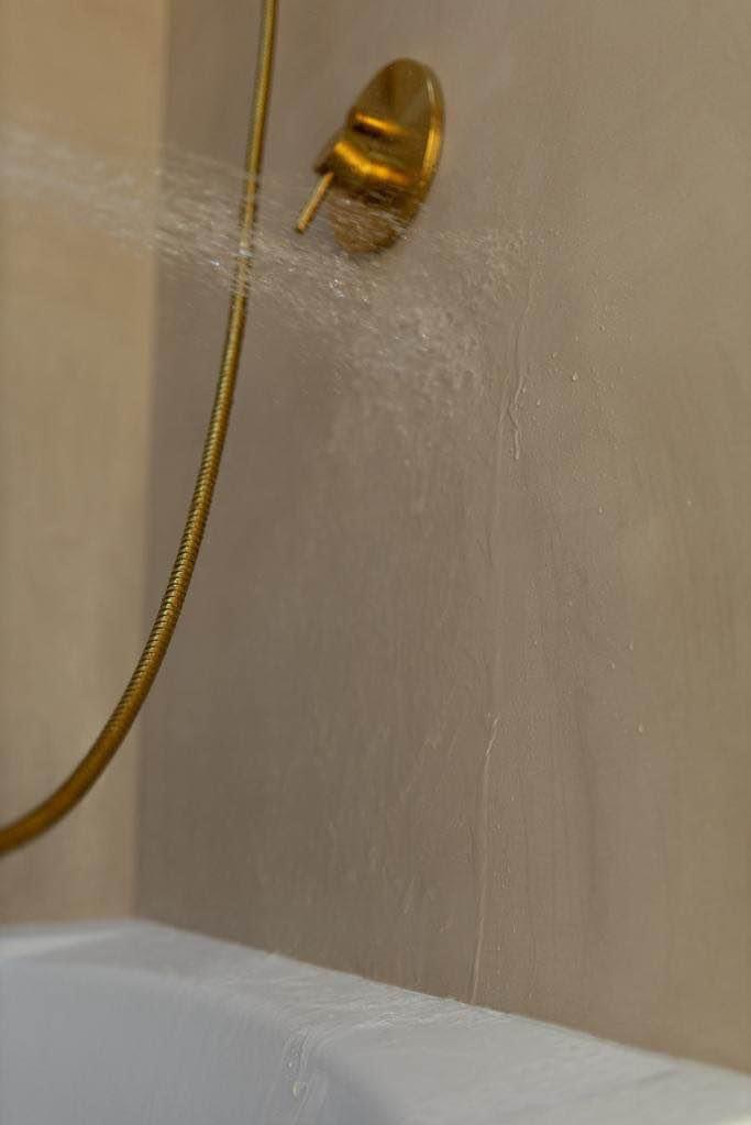 Świeżo położona gładź na ścianie łazienki z widocznymi śladami wilgoci od prysznica z mosiężną armaturą, tuż po zakończeniu prac.