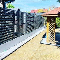 MEGIDO_Serwis - Nowoczesne ogrodzenie z poziomych, ciemnych desek i betonowej podmurówki, z widoczną drewnianą altaną z kratownicą w tle, w słoneczny dzień.
