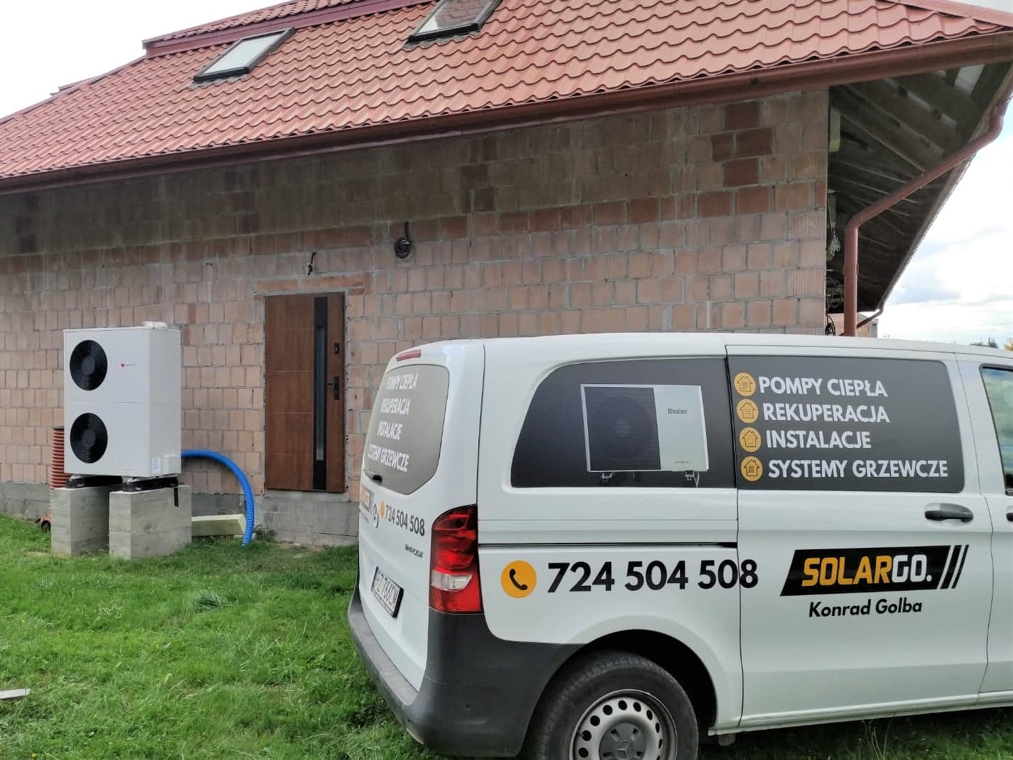 Biała pompa ciepła powietrze-woda zainstalowana na betonowych blokach przed domem z cegły, obok zaparkowany biały samochód dostawczy z reklamą firmy Solargo i hasłami: Pompy ciepła, Rekuperacja...