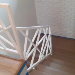 Biała, drewniana balustrada schodowa z geometrycznym wzorem na tle ściany z białej cegły i drewnianych schodów.