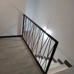 Nowoczesna czarna barierka schodowa z ukośnymi prętami, zamontowana na schodach z płytek imitujących drewno, widok z góry, surowy wystrój.