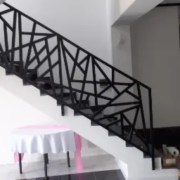 Nowoczesna, czarna balustrada schodowa o geometrycznym wzorze, widoczna z boku na tle białych ścian i ciemnych stopni, z dekoracyjnym stołem z białym obrusem w dolnej części kadru.