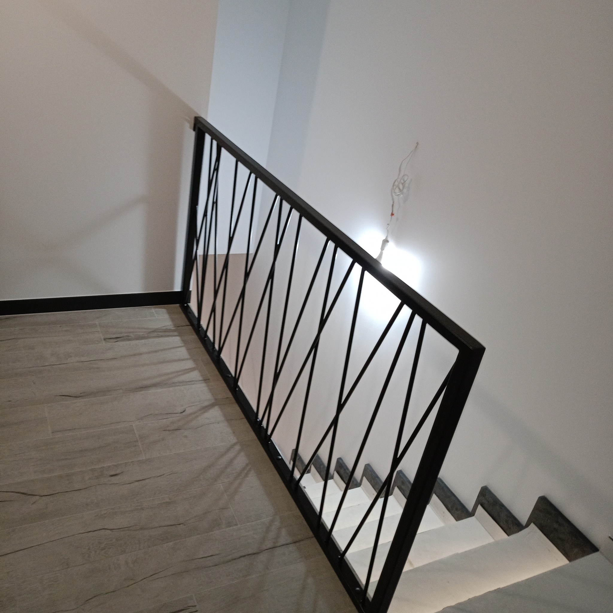 Nowoczesna czarna barierka schodowa z ukośnymi prętami, zamontowana na schodach z płytek imitujących drewno, widok z góry, surowy wystrój.