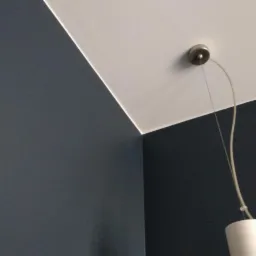 Fragment pomalowanego na ciemny grafit pokoju z białym sufitem i lampą wiszącą z kablem, widok na róg pokoju i łączenie ścian.