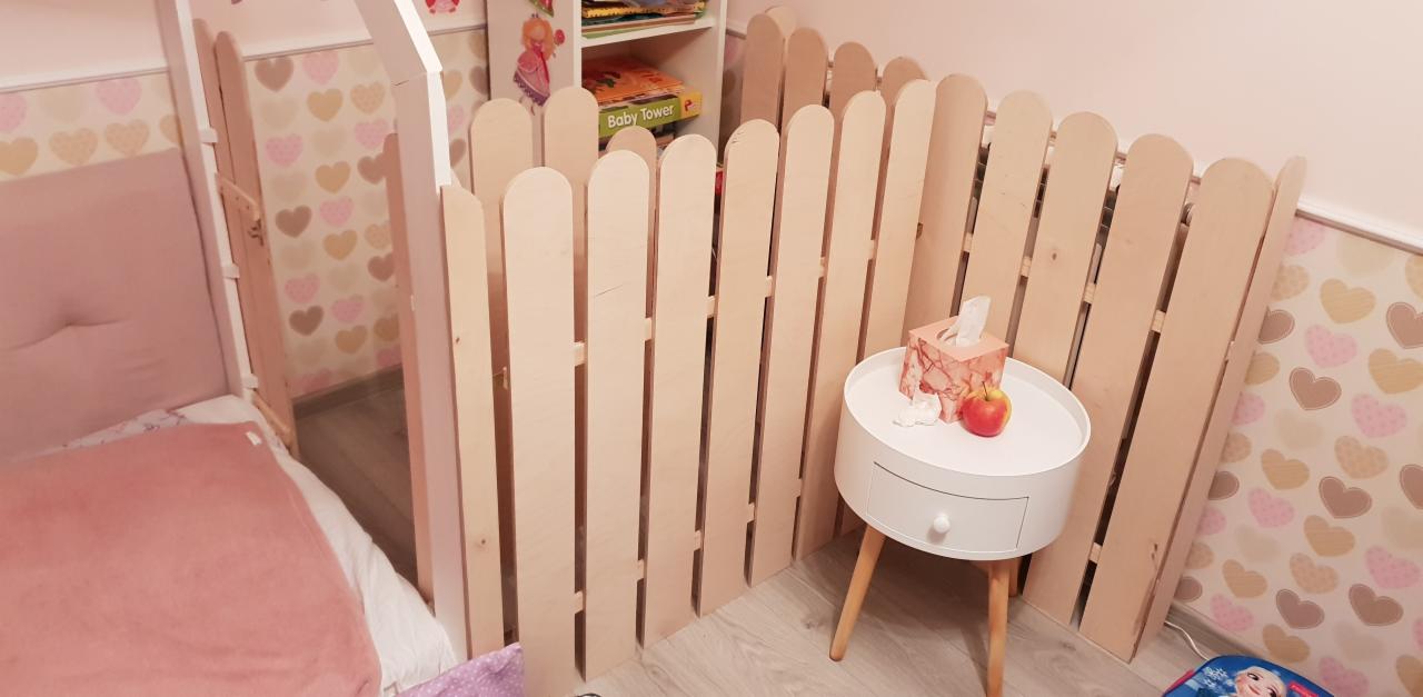 Drewniana antresola z barierką w pokoju dziecięcym, widoczna z boku, obok łóżka i szafki nocnej z jabłkiem i chusteczkami higienicznymi.