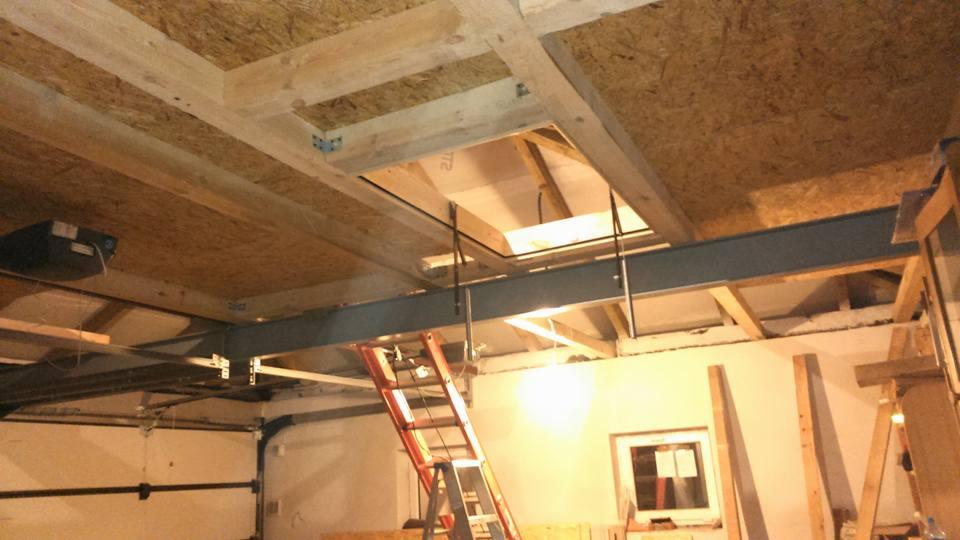 Konstrukcja stalowa wspierająca drewniany strop z otworem, widoczna drabina i fragment okna, garaż w trakcie przebudowy.