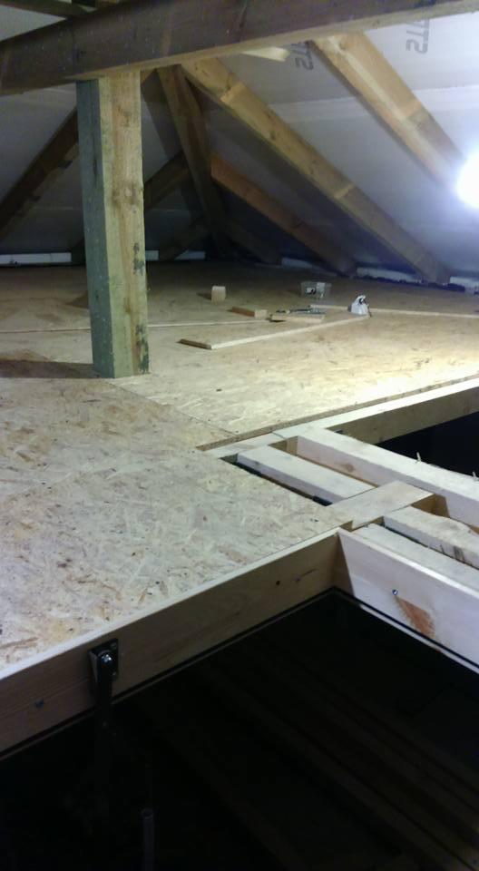 Wnętrze poddasza w trakcie adaptacji: drewniana konstrukcja antresoli z płyt OSB, widoczne elementy więźby dachowej i słup nośny.