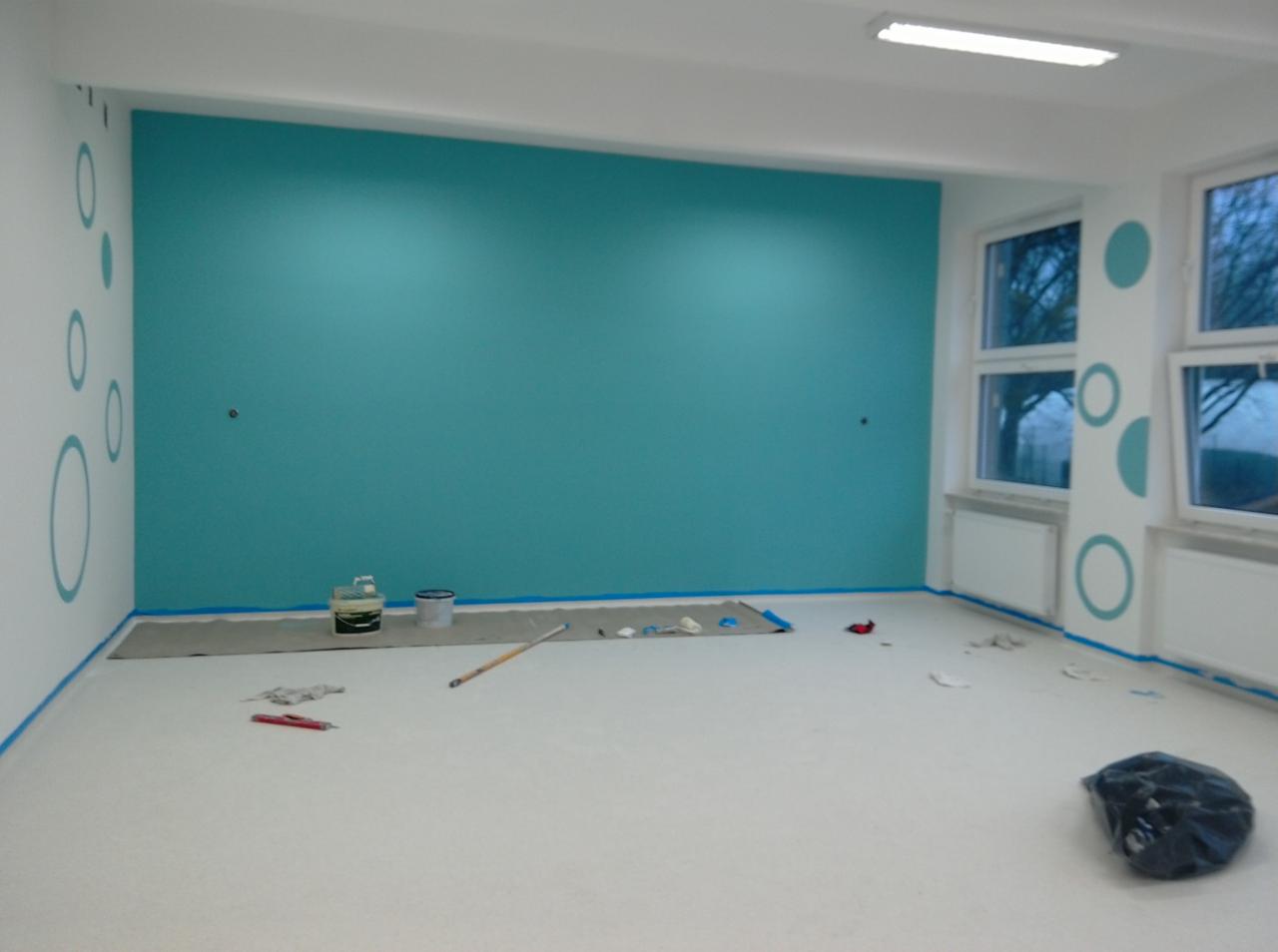 Świeżo pomalowane na turkusowo pomieszczenie biurowe z białymi ścianami i wzorami w kółka, widoczne narzędzia malarskie i zabezpieczenia podłogi.
