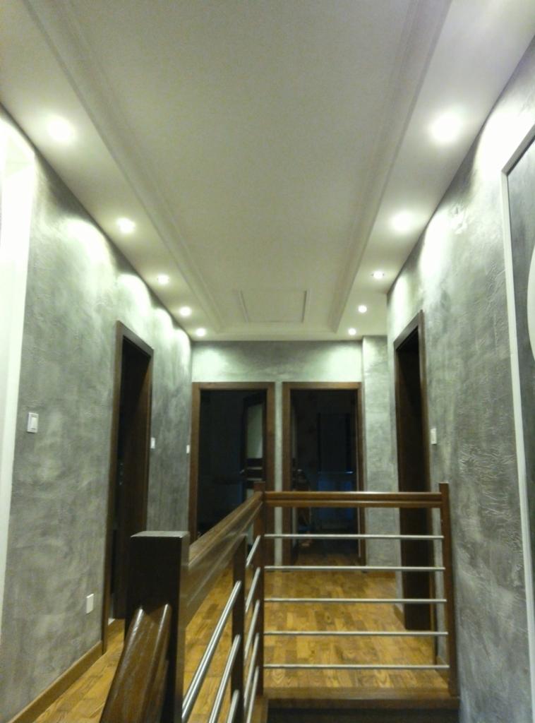 Korytarz po remoncie w domu w miejscowości Celiny Włościańskie, ściany wykończone w odcieniach szarości z efektem dekoracyjnym, drewniana podłoga i schody z metalowymi barierkami, oświetlenie...