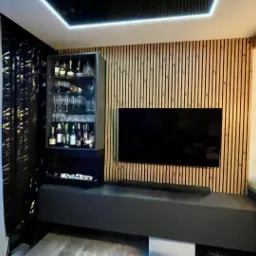 Nowoczesny salon z barkiem i telewizorem na tle drewnianej ściany z pionowych listew. Minimalistyczny design, oświetlenie LED i eleganckie wykończenie.