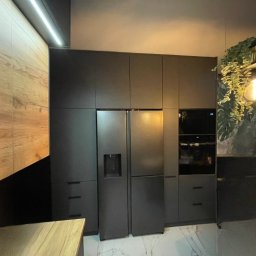 DJK Meble Sp. z o.o. - Ciemna zabudowa kuchenna z lodówką side-by-side i piekarnikiem, drewniane akcenty, marmurowe płytki podłogowe, oświetlenie dekoracyjne, nowoczesny design.