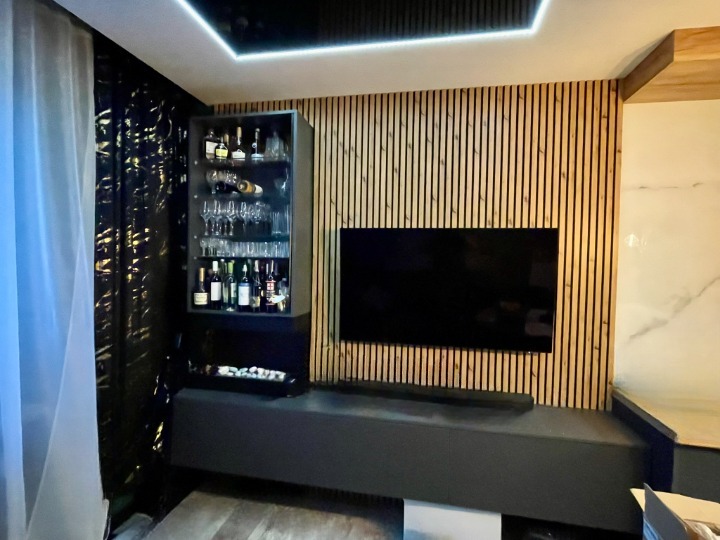 Nowoczesny salon z barkiem i telewizorem na tle drewnianej ściany z pionowych listew. Minimalistyczny design, oświetlenie LED i eleganckie wykończenie.